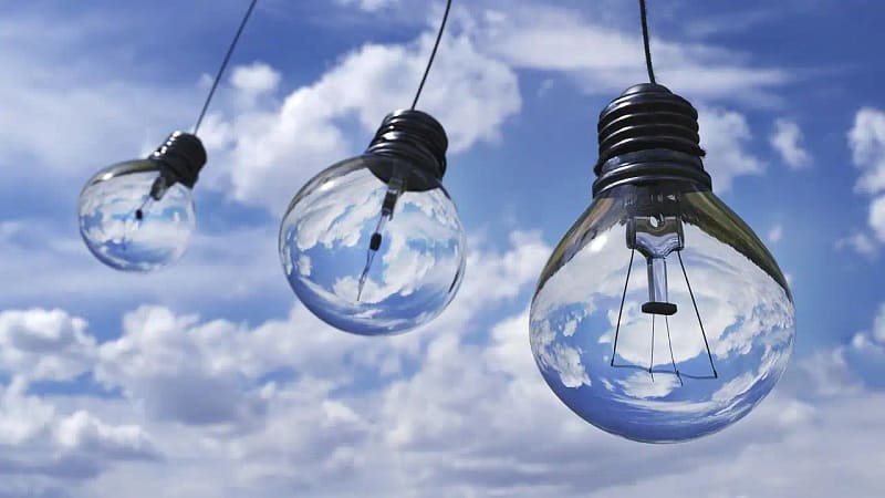 Tres bombillas colgantes reflejando un cielo con nubes, simbolizando ideas, claridad y reflexión más allá de la tecnología.